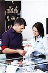 The seller in shop helps the man to pick up a jewel