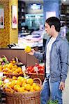 The young man holds an orange in shop