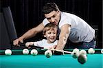 The young man learns the little boy to play billiards