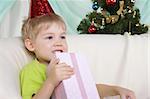 Little boy near to christmas fur-tree sits with gift