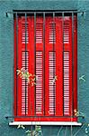 Red wooden window shutter and protective metal bars.