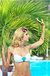 Beautiful woman near swimming pool under palm tree