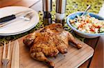 Whole cooked chicken on cutting board served with salad