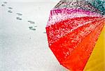 Colorful umbrella in the fresh snow with some footprints around it.