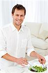 Joyful man serving salad standing at a table in the living room at home