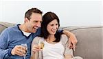Cheerful couple drinking champagne on the sofa while watching television