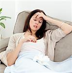 Sick woman looking at a thermometer while resting on the sofa at home