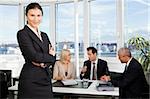 Businesswoman sitting in front. Three business colleagues working in background.