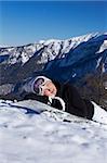 A girl in a ski suit in the mountains in winter laying on snowboard