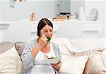 Pregnant woman eating vegetables on her sofa