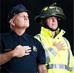 Policeman and fireman saying the pledge of allegiance.  Photographed on black background.