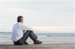 Thoughtful businessman sitting on a beach and looking at the sea