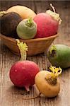 Group of ripe variegated radishes in rustic woven bowl on the old wooden board