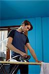 portrait of caucasian adult man ironing white shirt at home. Vertical shape, low angle view, side view, copy space