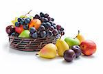 Various fresh ripe fruits placed in a wicker basket and around isolated on a white background