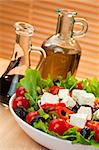 Fresh lettuce tomato pepper olive red onion and feta cheese salad with olive oil and balsamic vinegar dressing shot in warm summer sunlight