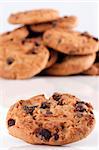 Close up of a chocolate chip cookie with a pile of chocolate chip cookies unsharp in the background on white