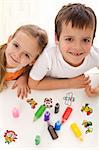 Two smiling happy kids painting with lots of colors in small bottles - top view