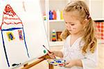 Little artist girl painting her dream house on large paper canvas