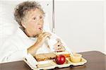 Senior woman in the hospital, eating lunch and drinking from a straw.