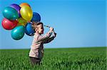 Happy boy with balloons running on the spring field.