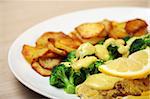 A close-up of fried cod with sliced potatoes, broccoli and bechamel sauce