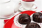 Delicious three chocolate cake on red plate with tea cup and teapot