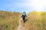 Hiker with rucksack up-hill at summer sunny day