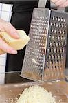 Parmesan cheese with grater on wooden chopping board.