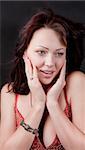 The young woman at the center of the frame. She is surprised and presses her hands to her face. On the one hand she has a bracelet. Black background.