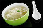 Chinese noodle soup in a green bowl with a white chinese ceramic spoon photographed on black with a reflection