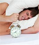 angry man stressed by his alarm clock lying on his bed at hom