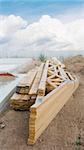 stack of wooden joists and building lumber at construction cite against a blue sky.