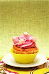 Fresh vanilla cupcake in green cup with strawberry icing and marshmallows on decorative background