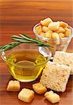 Two jars of olive oil with stick of rosemary and croutons on wooden table background