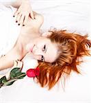 Beautiful red-haired girl with rose in the bedroom. Indoor shot.