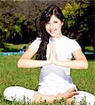 Beautiful young brunet yoga girl on green grass in park.