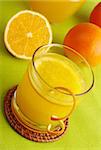 Fresh orange juice with orange slice in glass and oranges in background on green table mat (Selective Focus)