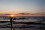 Silhouettes of father and his douther jumping and having fun on beach at sunset