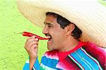 Mexican man poncho sombrero eating red chili hot pepper Mexico