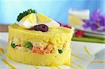 Traditional Peruvian dish called Causa made of mashed yellow and white potato mixed with aji (hot pepper) and lime juice and filled with vegetables (corn, peas, carrots) and mayonnaise and garnished with eggs and olives (Selective Focus, Focus on the front)