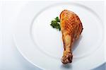 Closeup picture of roasted chicken leg on the white plate.