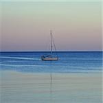 Sailboat reflected on sea water. Sunset sea and sky horizon.