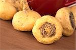 Peruvian Ginseng (Sp. Maca, lat. Lepidium meyenii) which is widely used in Peru for its various health effects and high nutritional value with a red tea cup in the back on wood (Selective Focus, Focus on the front root)