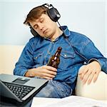 A young man fell asleep at home on the couch with a beer