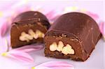 Two pecan nut truffle halves surrounded by pink petals (Selective Focus, Focus on the upper right corner of the pecan nut filling in the right truffle half)