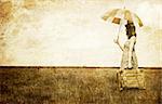 Redhead enchantress with umbrella and suitcase at spring wheat field. Photo in old image style.