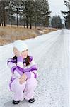 Young girl sitting in the middle of a long isolated road