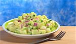 Potato salad with green and red onions and cucumber with a mayonnaise-cream dressing garnished with blue background (Selective Focus, Focus on the front of the salad)