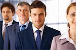 Young serious businessman standing in the row with his colleagues.